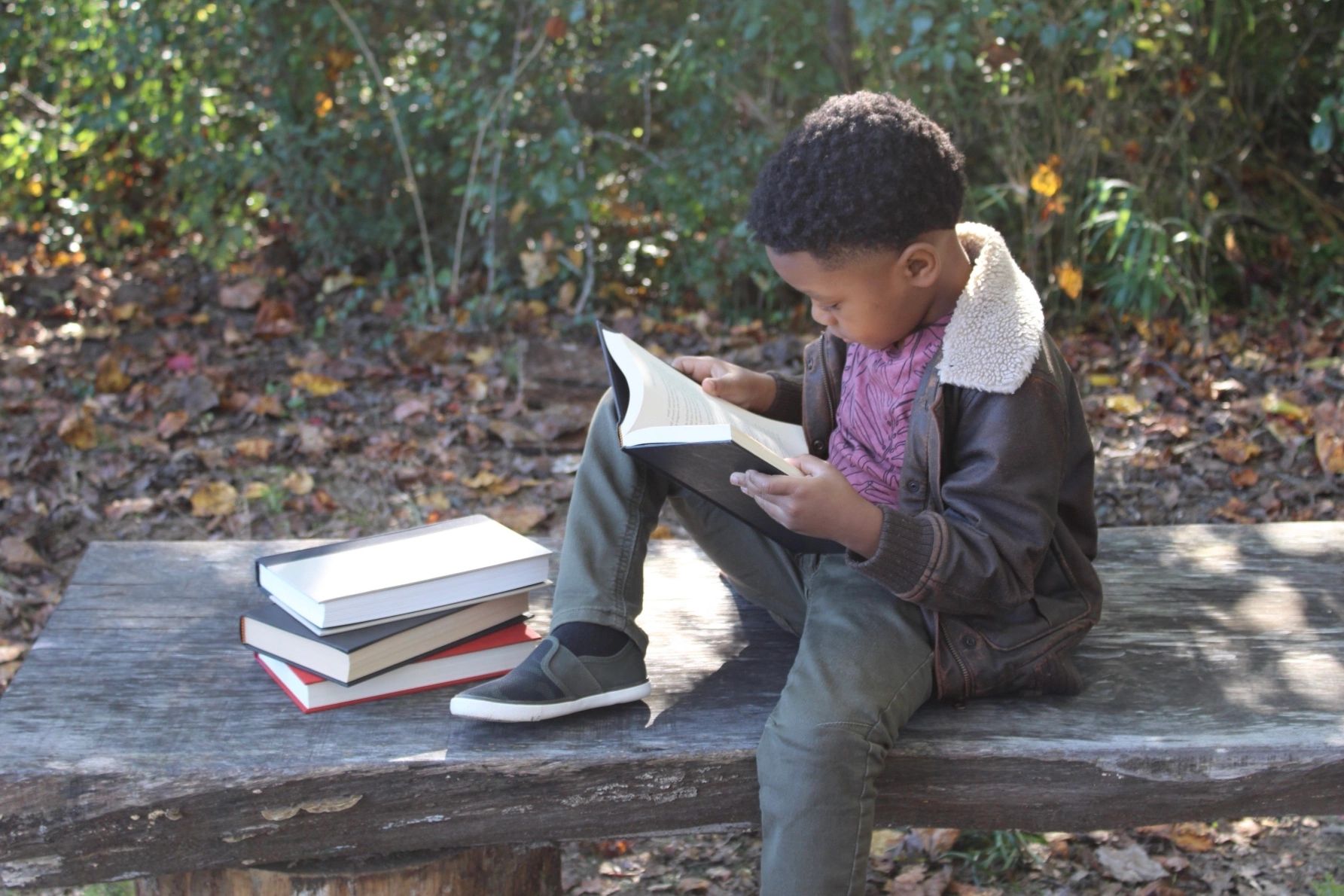 A young child reading outdoors on a wooden bench